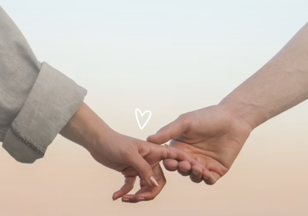 Two people reaching for each other and joining hands against a warm evening sky