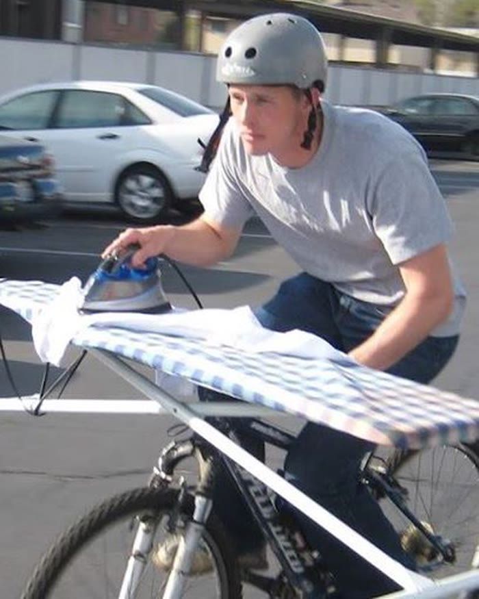 Cooper, Co-founder of Mutual, riding a bicycle while ironing a shirt on an ironing board balanced across the handlebars